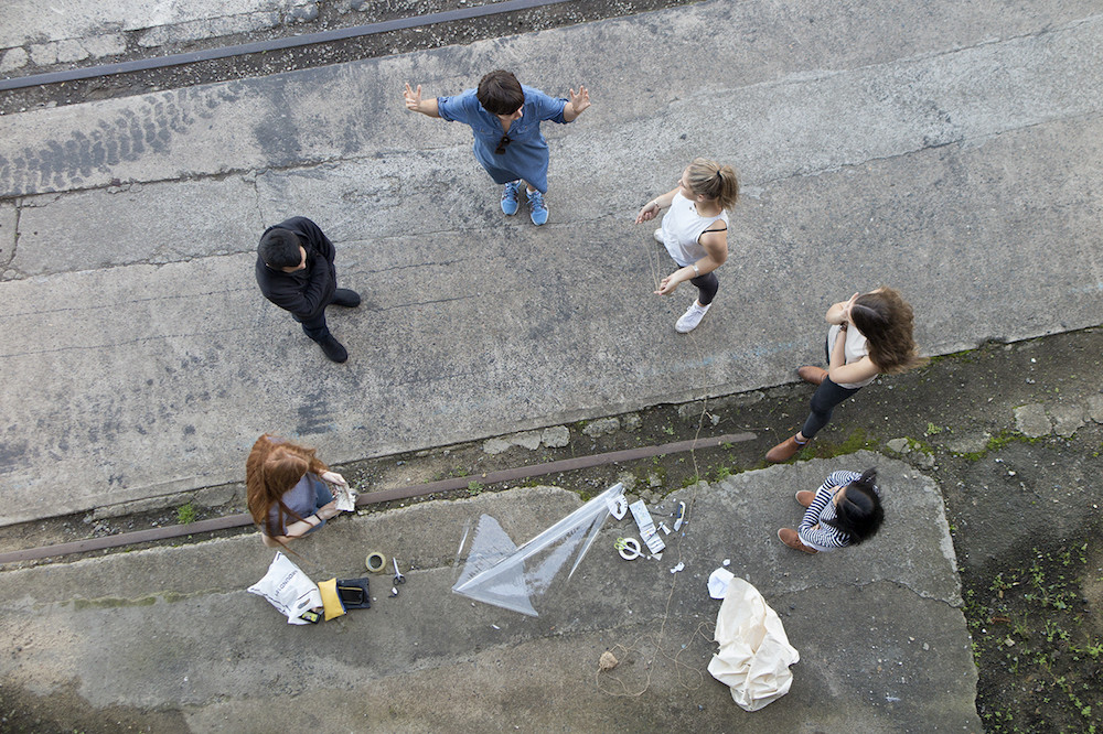 Top down shot of Clare Cooper and a group of workshop participants outside, materials at their feet